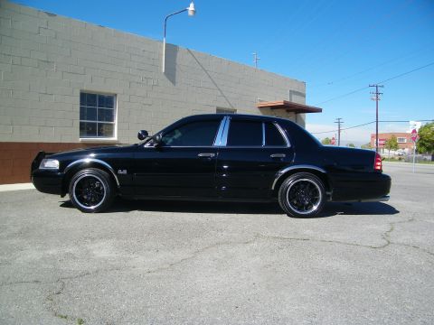 2003 Ford Crown Victoria - Full side view of blacked-out sedan with chrome pillar trim against blue sky