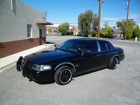 2003 Ford Crown Victoria - Blacked-out sedan on dark wheels with push-bar guard parked beside gray building