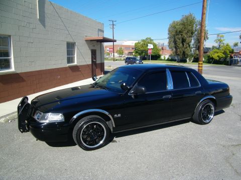 2003 Ford Crown Victoria - Blacked-out four-door sedan on dark rims with push-bar guard, street and trees behind
