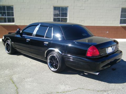 2003 Ford Crown Victoria - Blacked-out sedan rear quarter showing red taillights, chrome trim and dual tips