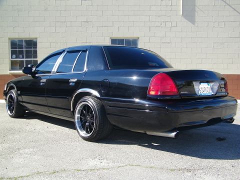 2003 Ford Crown Victoria - Blacked-out sedan rear view on dark rims with chrome rocker trim and dual exhaust