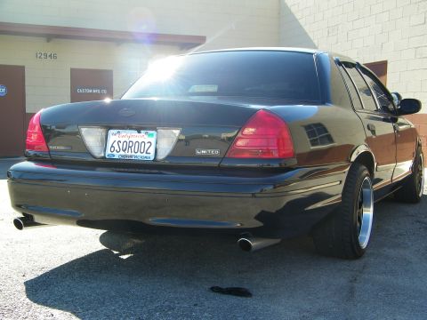 2003 Ford Crown Victoria - Sun-lit rear view of a black Crown Victoria sedan, Ford oval and Limited trunk badges visible.