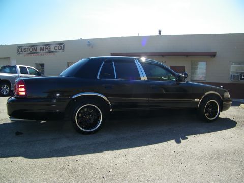 2003 Ford Crown Victoria - Side profile of lowered black Crown Victoria on dark wheels outside an industrial shop.