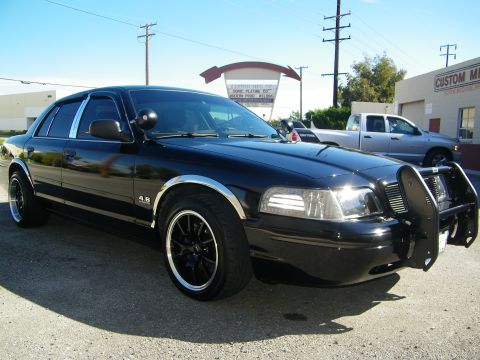 2003 Ford Crown Victoria - Sunlit front view of black Crown Victoria with grille guard and aftermarket black wheels.