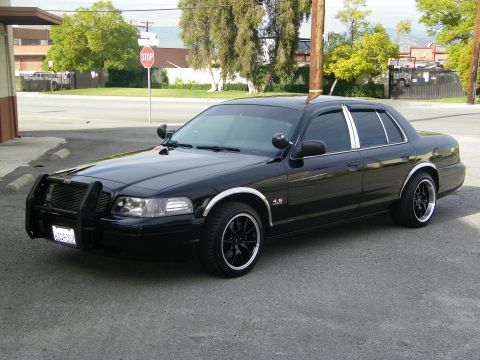 2003 Ford Crown Victoria - Black Crown Victoria with chrome window trim and dark machined wheels parked at a curb.