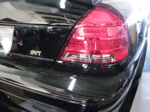 2003 Ford Crown Victoria - Detail of a red taillight lens and SVT emblem on a glossy black trunk lid.
