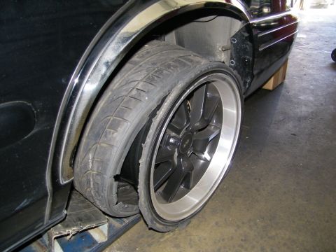 2003 Ford Crown Victoria - Delaminated tire with tread separating from a polished-lip gunmetal wheel inside a wheel well.