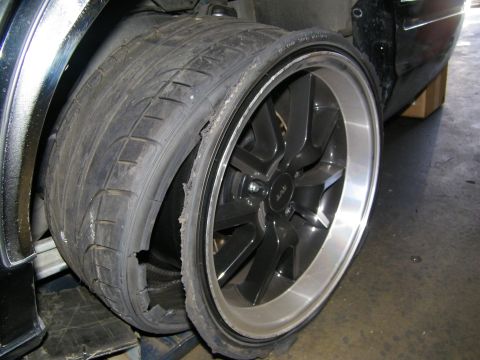 2003 Ford Crown Victoria - Tire failure showing rubber tearing away from a multi-spoke alloy wheel mounted on a dark vehicle.