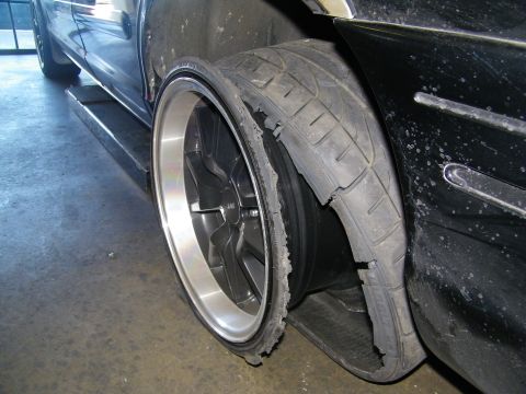 2003 Ford Crown Victoria - Low-angle view of a disintegrating tire wrapped around a polished-lip alloy wheel on a black car.