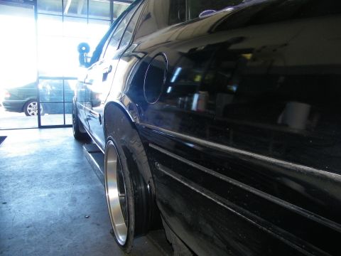 2003 Ford Crown Victoria - Glossy black bodyside and fuel-filler door with a polished deep-lip wheel inside a shop.