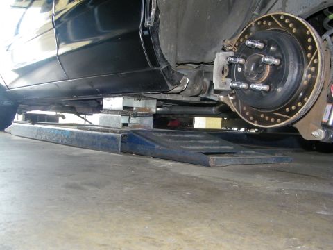 2003 Ford Crown Victoria - Exposed wheel hub studs and cross-drilled rotor on a lowered black car over a steel ramp.