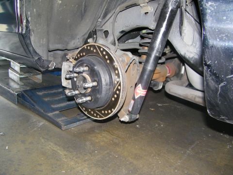 2003 Ford Crown Victoria - Undercarriage view of rear hub, drilled rotor and shock on a black car raised on a ramp.