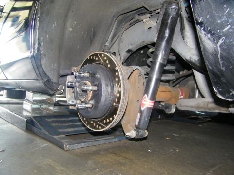2003 Ford Crown Victoria - Black car undercarriage showing hub studs, drilled rotor, coil spring and rear shock.