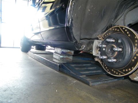 2003 Ford Crown Victoria - Low-angle undercarriage view of rear hub and cross-drilled rotor over a steel ramp.