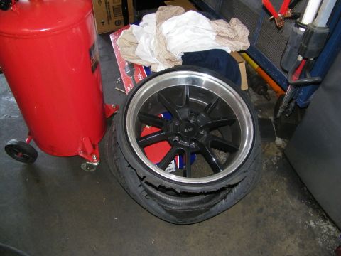 2003 Ford Crown Victoria - Aftermarket LAS wheel wrapped in a destroyed tire on a shop floor next to an air compressor.