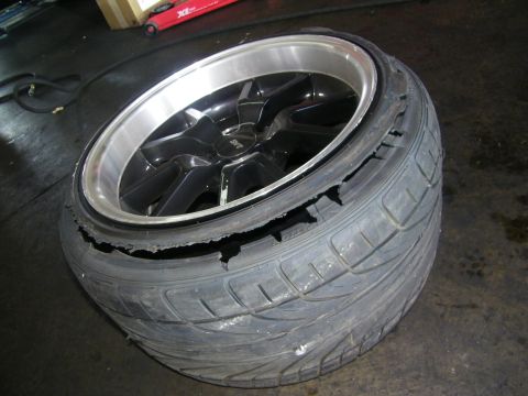 2003 Ford Crown Victoria - Multi-spoke alloy wheel mounted in a tire that is tearing apart, resting on the floor.