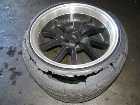 2003 Ford Crown Victoria - Polished-lip LAS alloy wheel inside a badly damaged tire on a shop floor.