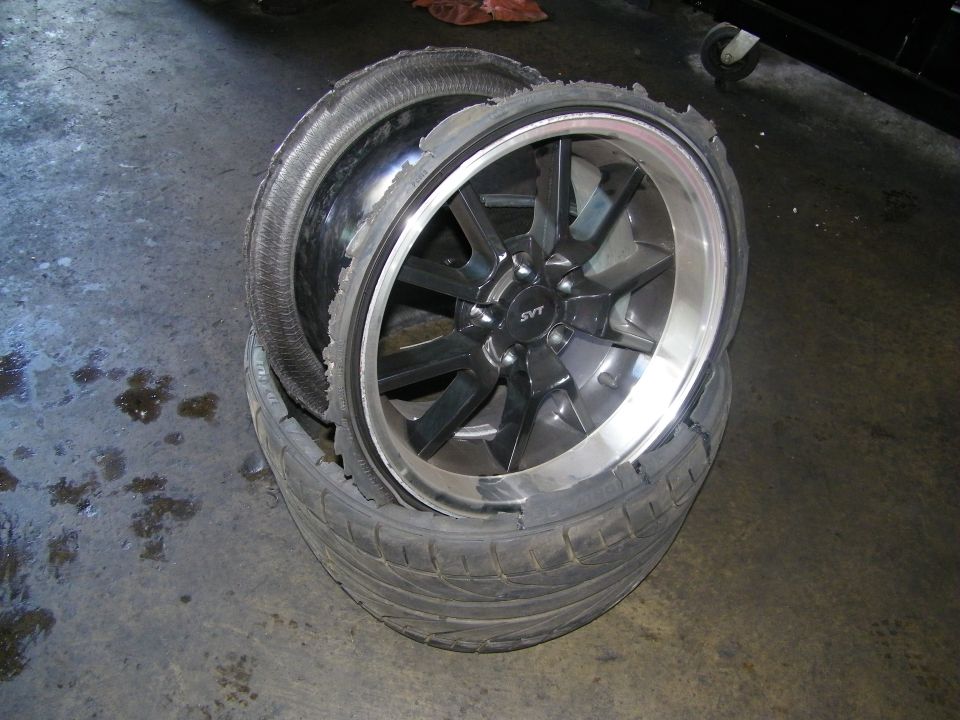 Two SVT gunmetal alloy wheels with shredded tires stacked on shop floor