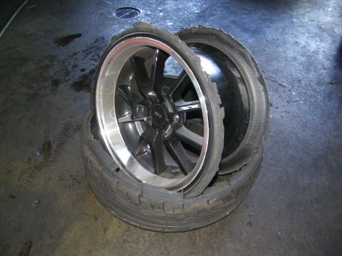 2003 Ford Crown Victoria - Two SVT-branded alloy wheels with shredded tires resting on a damp shop floor.