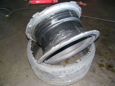 2003 Ford Crown Victoria - Stripped wheel barrel separated from its torn tire lying on concrete in a garage.