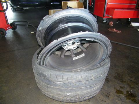 2003 Ford Crown Victoria - Pair of wheels with shredded tires on a garage floor next to a red rolling tool chest.
