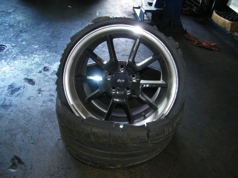 2003 Ford Crown Victoria - Polished-lip SVT alloy wheel wrapped in a destroyed tire resting on concrete.