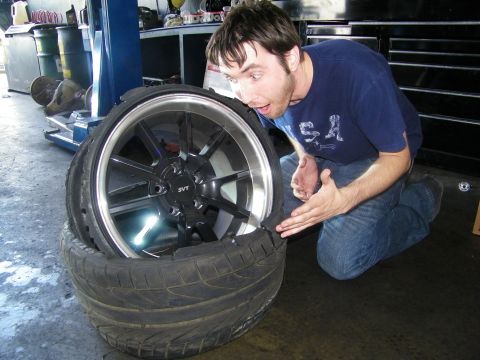 2003 Ford Crown Victoria - Garage scene: a man inspects a chrome-lipped SVT-centered alloy wheel mounted on a wide tire
