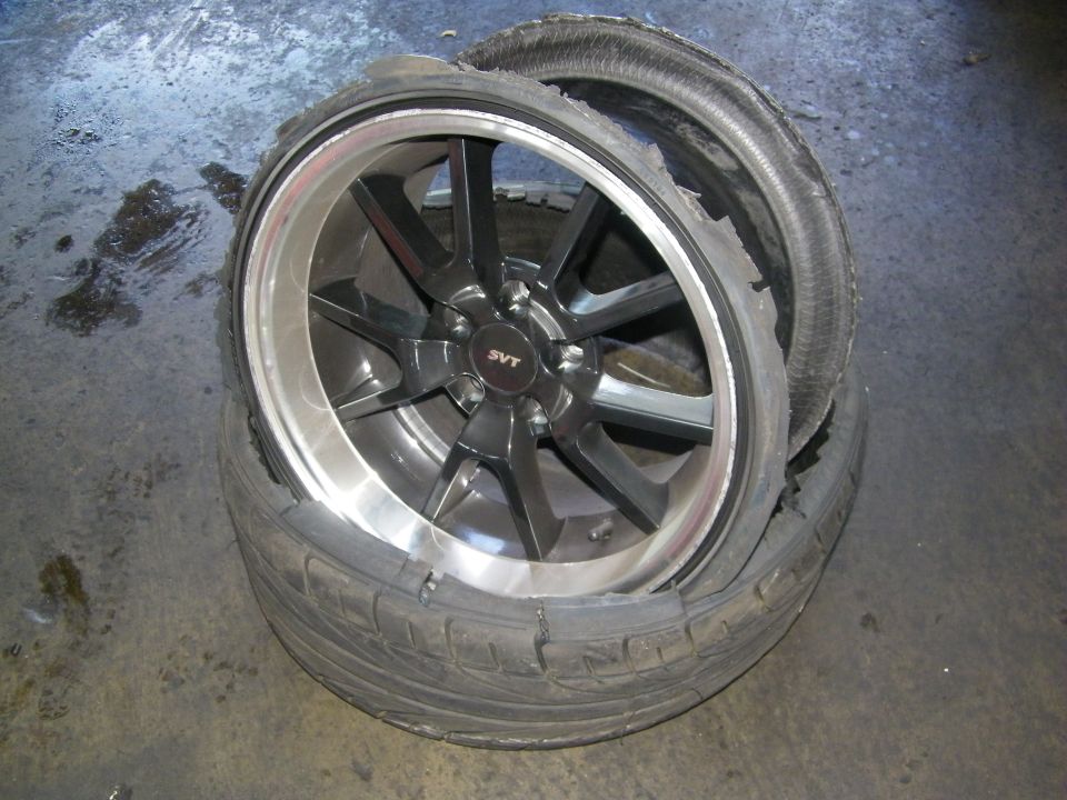 Black SVT-center alloy wheel with shredded low-profile tire on shop floor