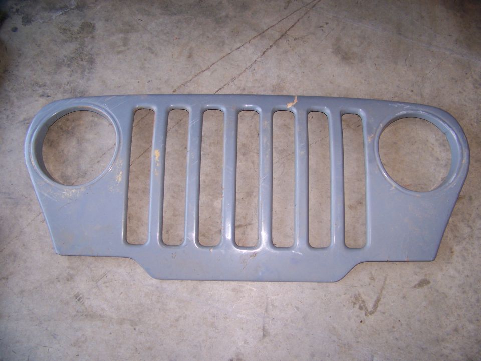 Gray Jeep grille with seven vertical slots and two circular headlight cutouts. Supermotors.net logo at bottom right