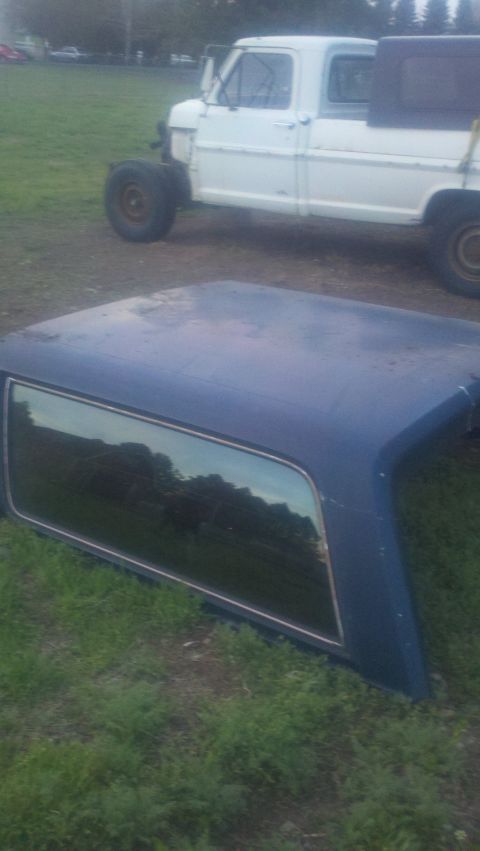 1988 Ford Bronco - A blue truck bed cap rests on the grass in front of a white pickup truck.