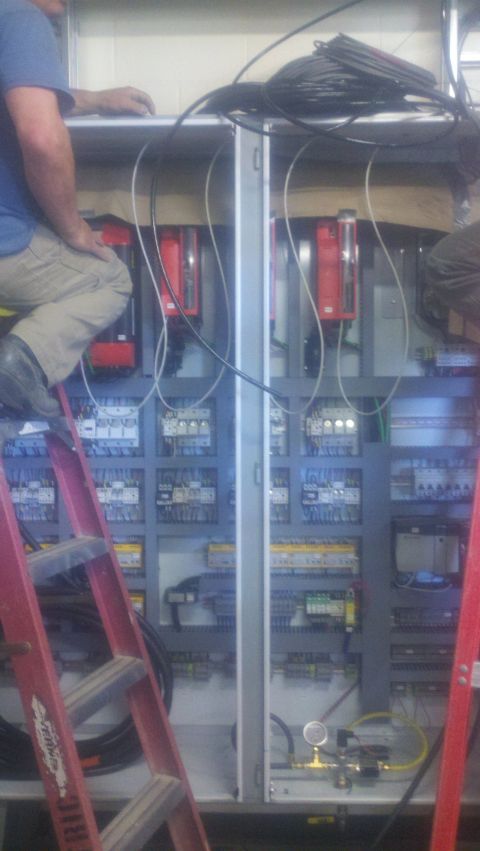 1988 Ford Bronco - Workers install and wire an electrical control panel with multiple red components and numerous switches.
