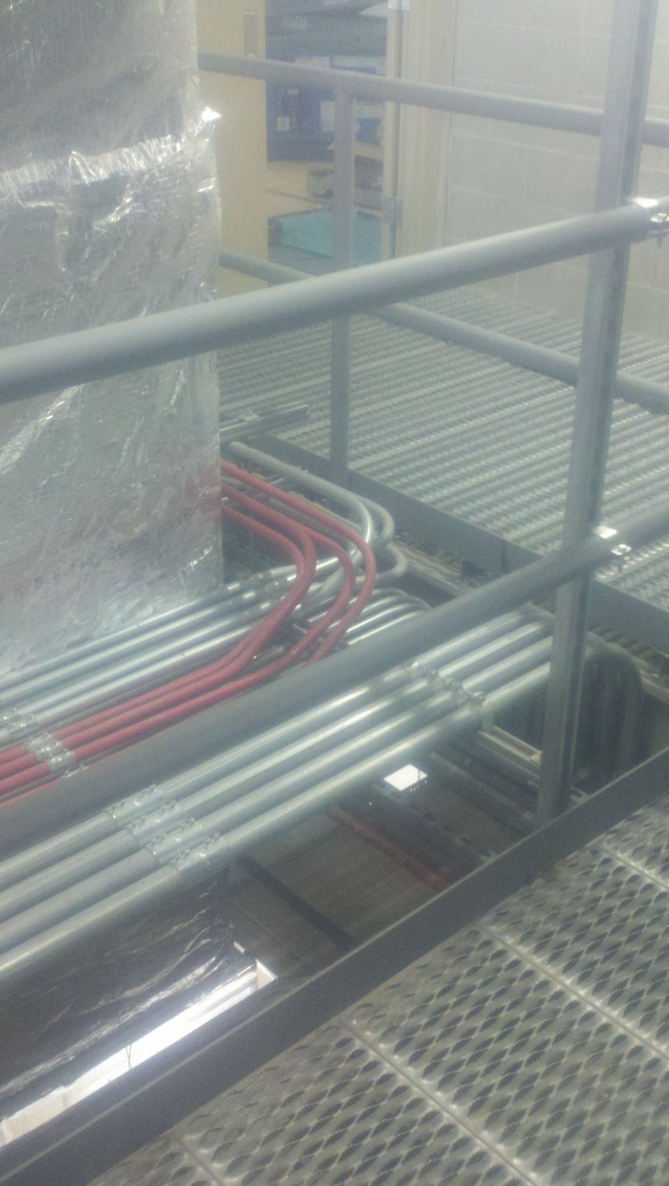 Industrial grating and pipes, some red, some silver, wrapped in plastic