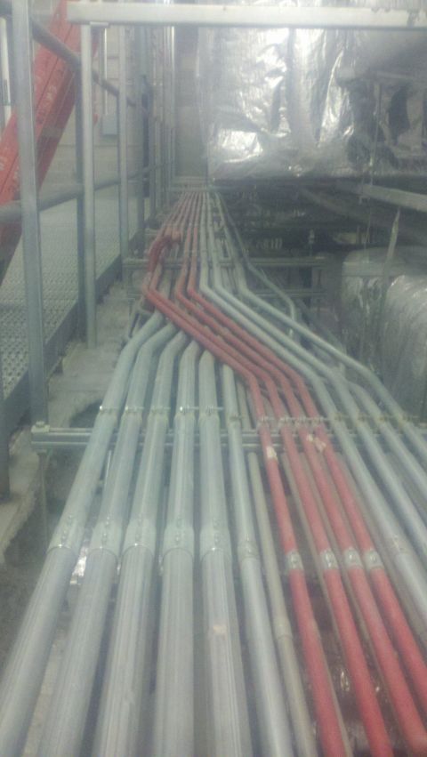 1988 Ford Bronco - Industrial pipes are organized along a metal walkway, with some pipes painted red and others gray.