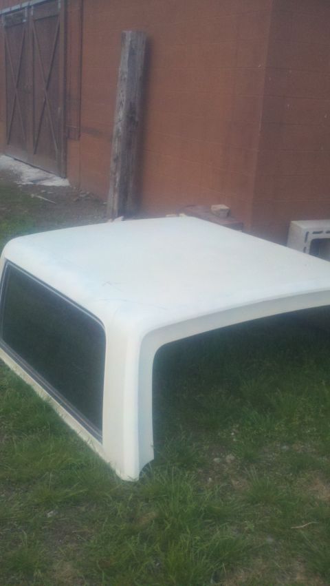 1988 Ford Bronco - White camper shell with tinted windows, resting on grass in front of a brick building.