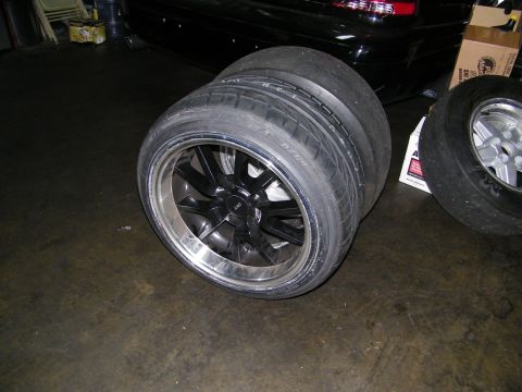 2003 Ford Crown Victoria - Pair of polished-lip alloy wheels on wide tires staged near a black sedan indoors