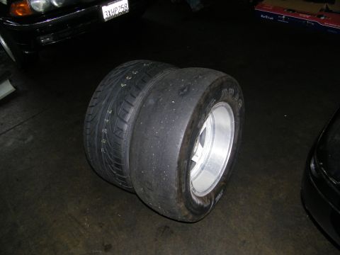 2003 Ford Crown Victoria - Two mounted wide tires, one a balding slick, on silver wheels in a dim garage