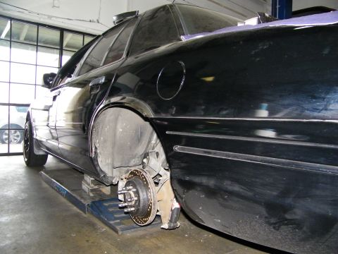 2003 Ford Crown Victoria - Black sedan on a shop alignment lift with front hub and brake rotor exposed