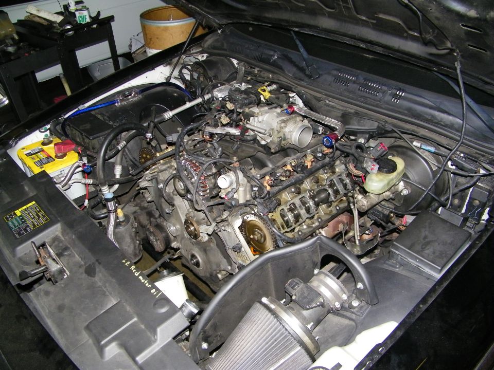 V8 engine bay with valve covers removed exposing cylinder heads during teardown