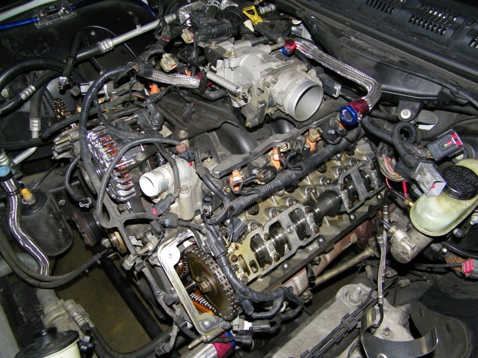 Disassembled V8 engine showing exposed valvetrain timing chain and throttle body