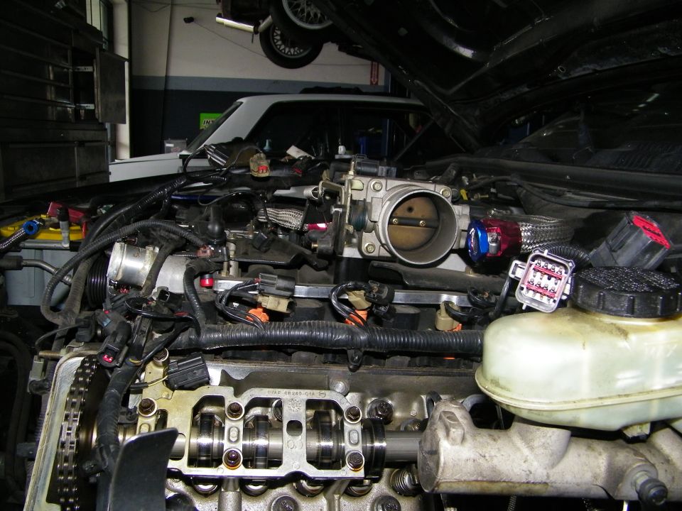 Engine bay with throttle body and exposed valvetrain under raised hood in shop