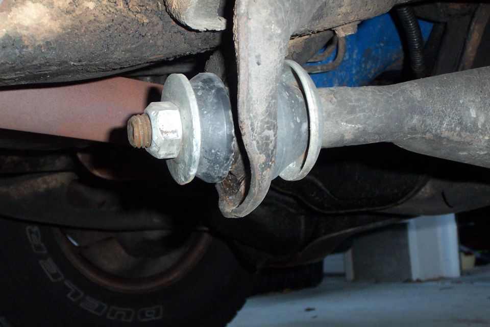 Underside close-up of suspension bushings and hex nut on a link, Dueler tire behind