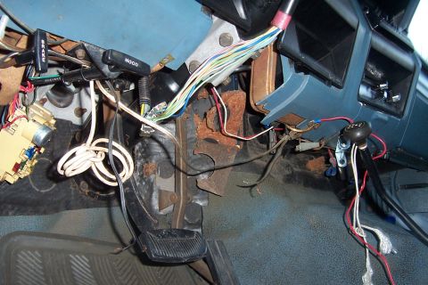 1980 Ford Bronco - The dashboard and floor of a vehicle are visible, with many wires exposed and disconnected.
