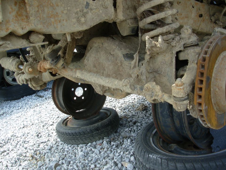 Muddy front axle and suspension resting on stacked wheels over gravel