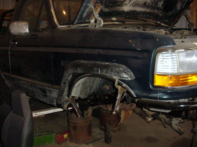 Dark green Ford Bronco on buckets with front wheel and suspension removed in a shop