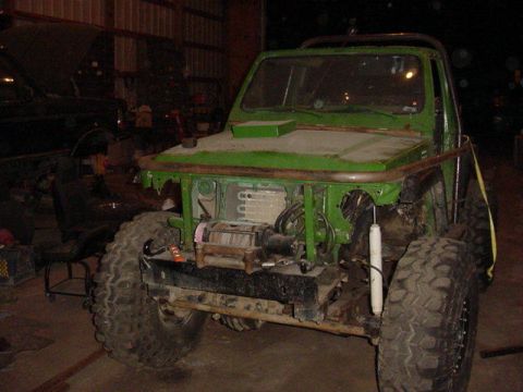 1992 Ford Bronco - A green, heavily modified off-road vehicle sits in a workshop with another vehicle partially visible in the background.