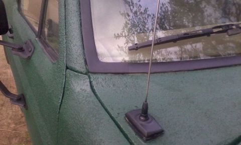 1986 Ford Bronco - Close-up of a green vehicle's textured exterior, showing the door seam and windshield area.