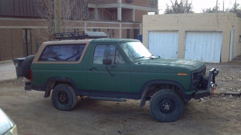 1986 Ford Bronco - This 1986 Ford Bronco features a tan removable top, roof rack, and a spare tire mounted on the tailgate.