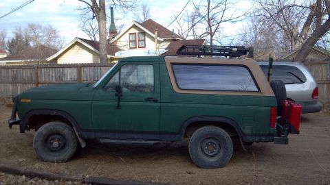 1986 Ford Bronco - This 1986 Ford Bronco is seen from the side, equipped with a roof rack and a rear-mounted spare tire carrier.