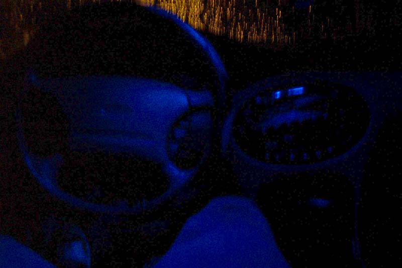 Dark interior shot of car steering wheel and gear shifter with blue ambient light
