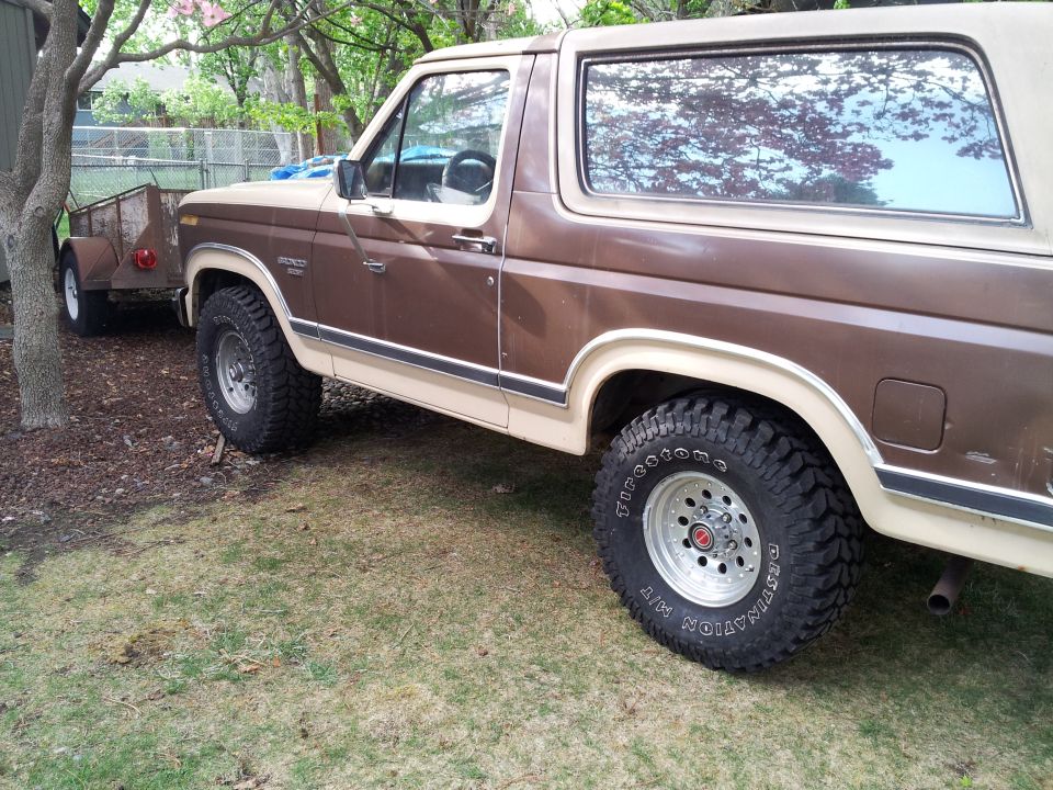 Brown two-tone Ford Bronco with aftermarket wheels and tires, parked on grass next to a small utility trailer